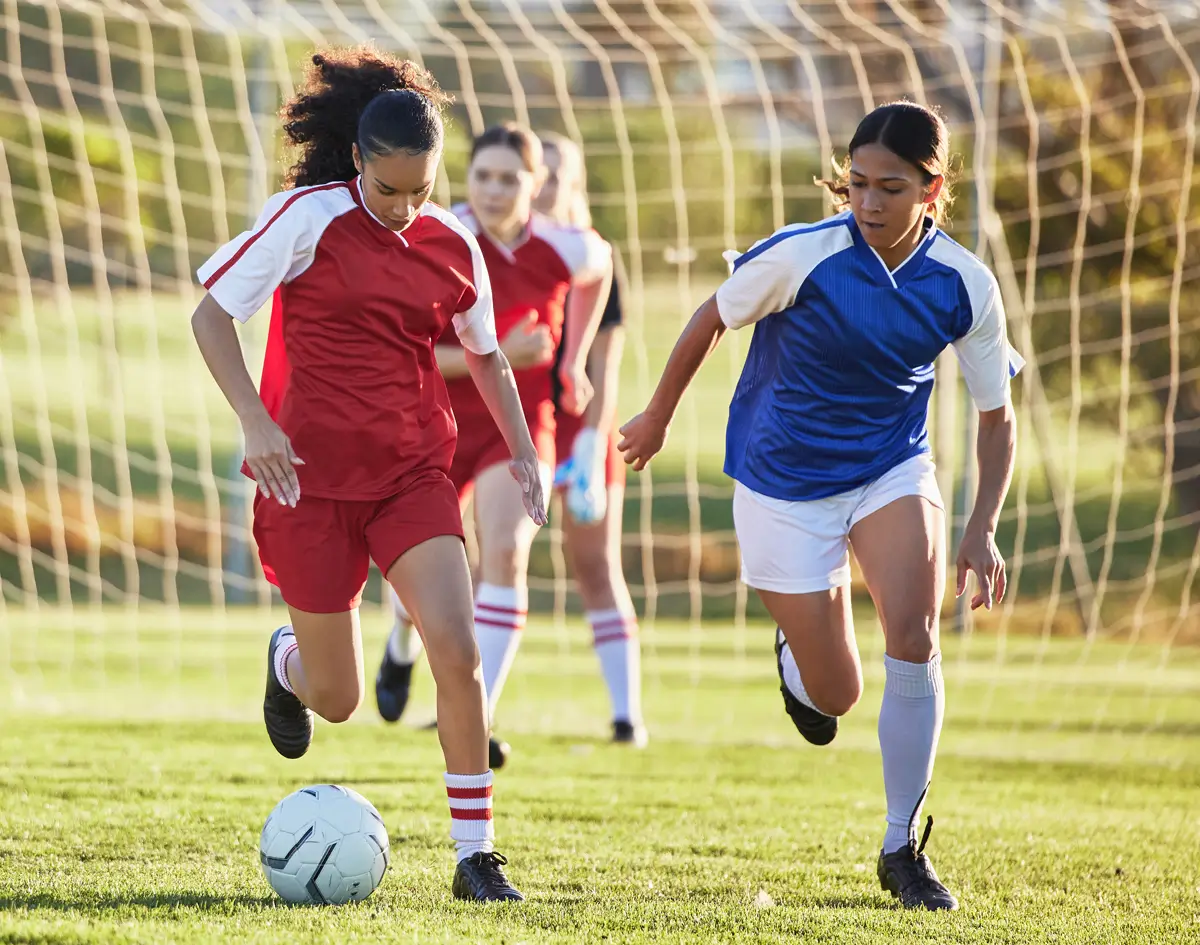 young athlete female football players kicking a ball on the pitch